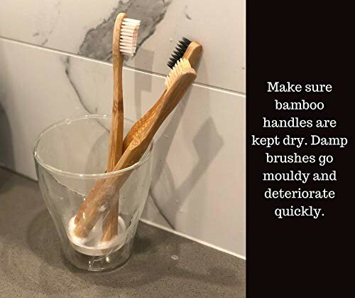 Two bamboo toothbrushes in a glass on a bathroom counter with a reminder to keep handles dry.