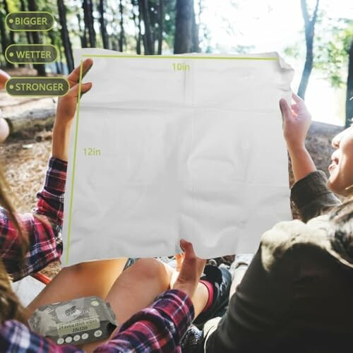 Two people holding a large white towel in a forest setting, showcasing its size.