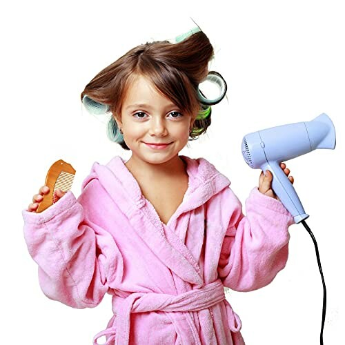 Child in pink robe holding hairdryer and comb.