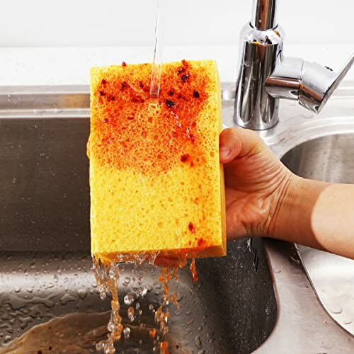 Hand rinsing a dirty sponge under running water in a sink