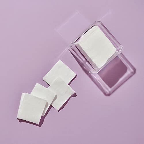 Cotton pads and a clear container on a purple background