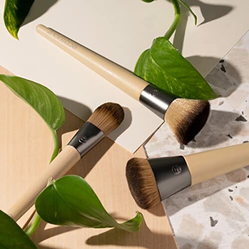 Makeup brushes on a wooden surface with green leaves.