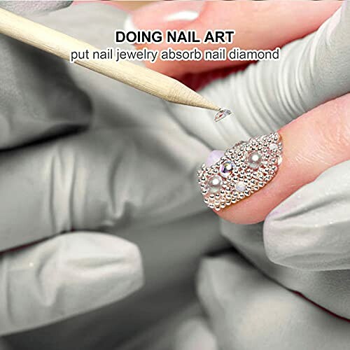 Close-up of gloved hands applying nail art with jewels.