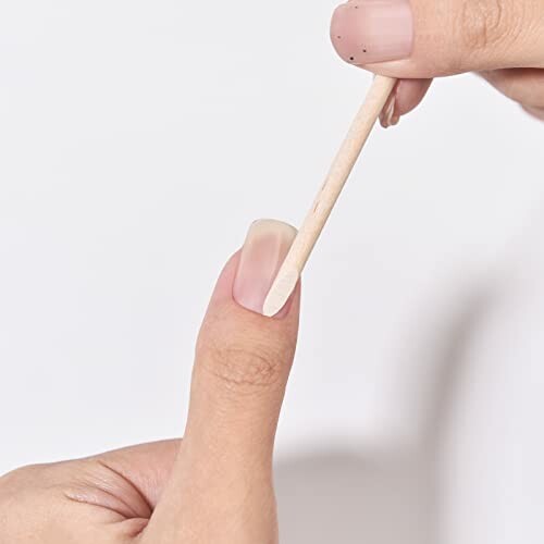 Person using a wooden cuticle pusher on a thumb nail