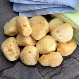 Natural sea sponges with folded towels on a wooden surface.