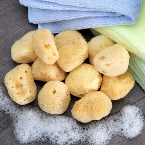 Natural sea sponges with towels and soap suds on wooden surface.