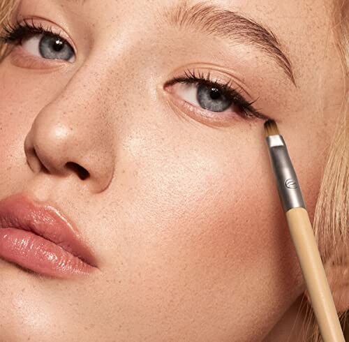 Close-up of a woman applying eyeliner with a brush.