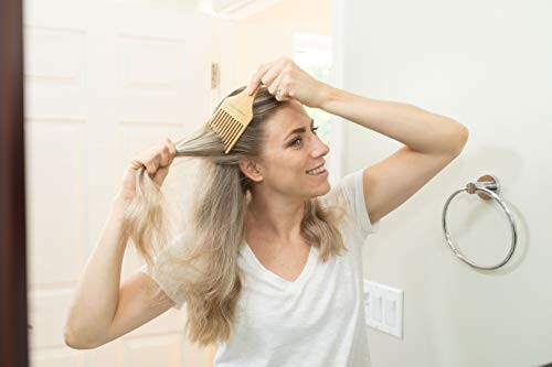 Woman combing her long hair in front of a bathroom mirror.