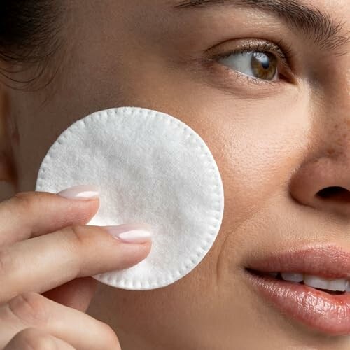 Close-up of a woman using a cotton pad on her face.