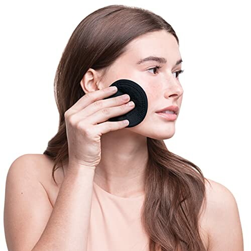 Woman using a black makeup remover pad on her face.