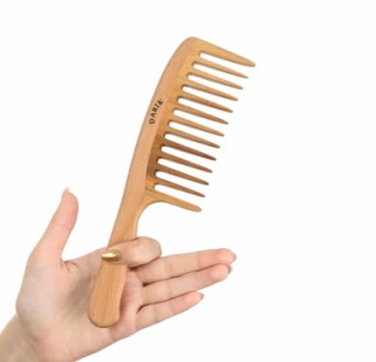 Hand holding a wooden wide-tooth comb with a curved handle.